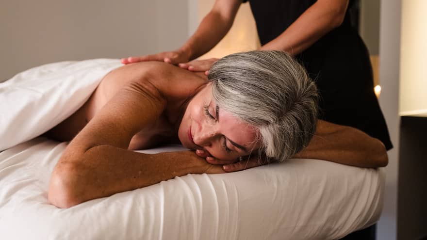 Person lies face down on massage table as therapist in black uniform performs massage