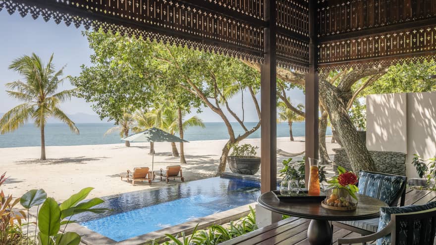 View of pool, beach and sea from covered terrace lounge