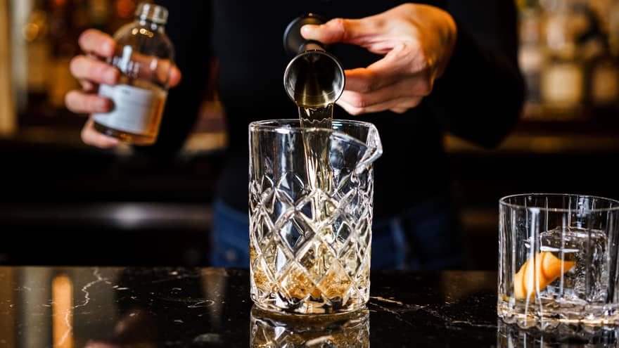 Person pouring a drink into a glass, with an empty glass beside it.