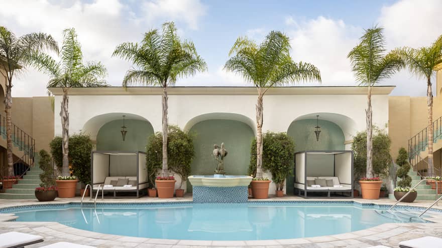A pool with lounge chairs and two daybeds as well as palm trees