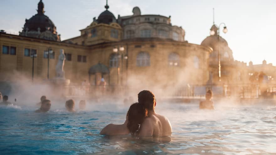 Couple huddled together in thermal pool at Szechenyi Thermal Baths in Budapest, other bathers in background