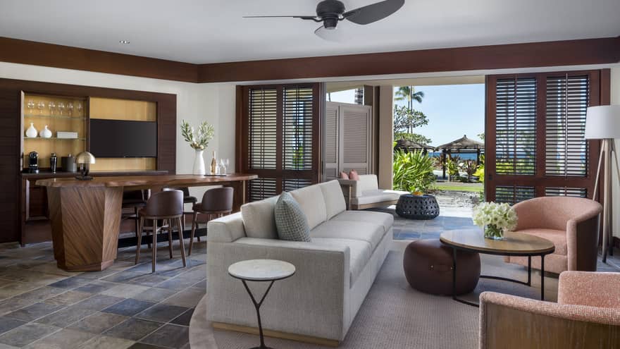 Suite's living room, with light grey sofa, two arm chairs, dining table, ceiling fan and walk-out terrace