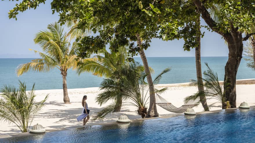 View of a woman walking on a tropical beach from a private pool