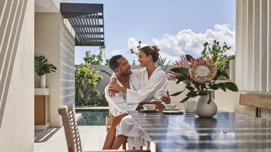 A couple is embracing at an outdoor dining table in a private villa at a beachside resort.