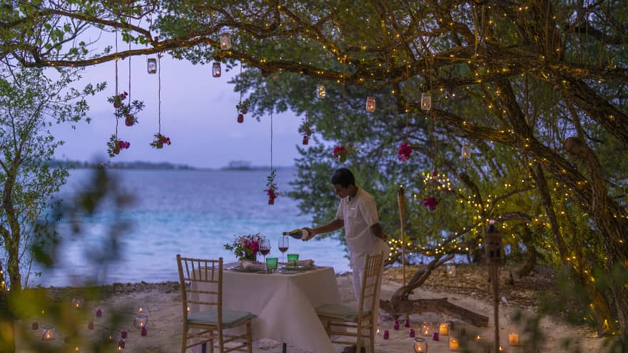 Resort staff pours wine into glass on beachside table set for two