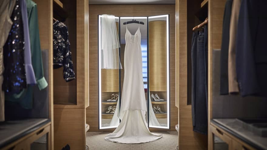 A wedding dress next to mirror in a large closet.