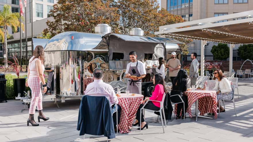 Outdoor venue with tables with red table cloths and the chef visiting a table.