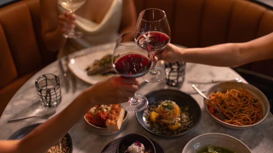Three guests raising their glasses at a dining table with culinary dishes