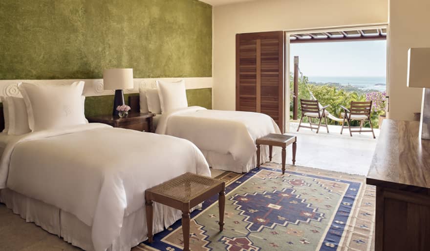 Bedroom with two twin beds, green accent wall, small benches, walk-out terrace