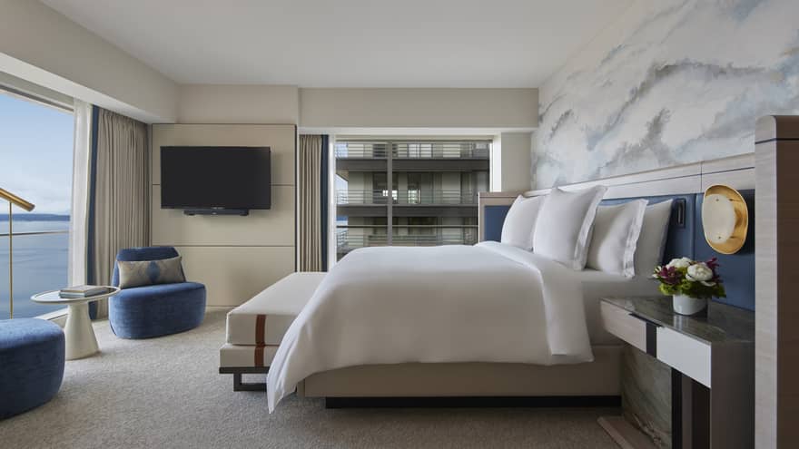 Bedroom with king bed, cloud-like accent wall, two royal blue chairs and wall of windows