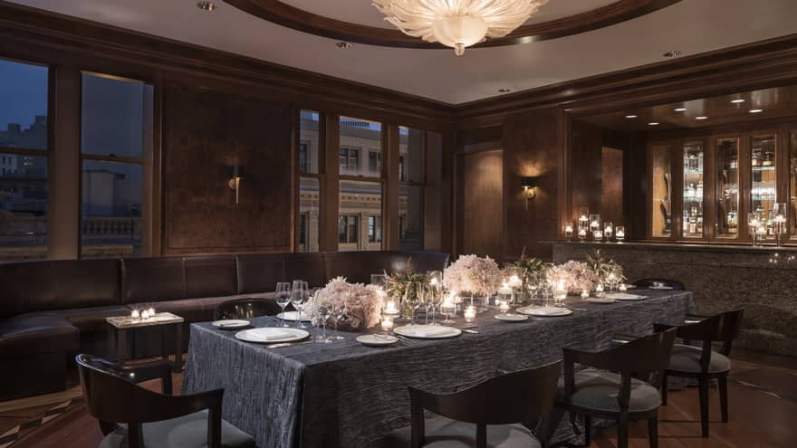 Elegant, candle-lit dining table in private den with grey tablecloth, pink flower arrangements, wine glasses