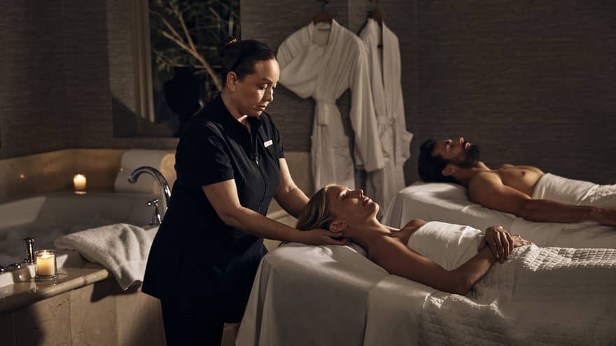 Two guests laying on massage tables in a room with a spa tub.
