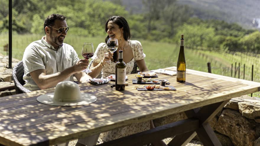 Two guests sitting outside at a picnic table holding wine glasses.
