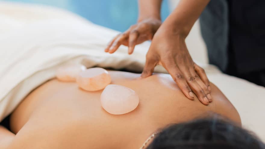Masseuse places salt stones on a person's bare back