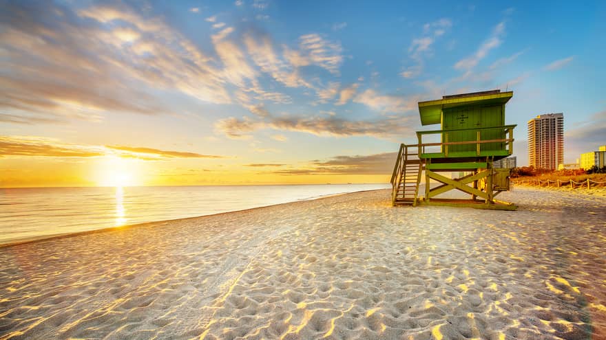 The sun rises over a green wooden building on the beach