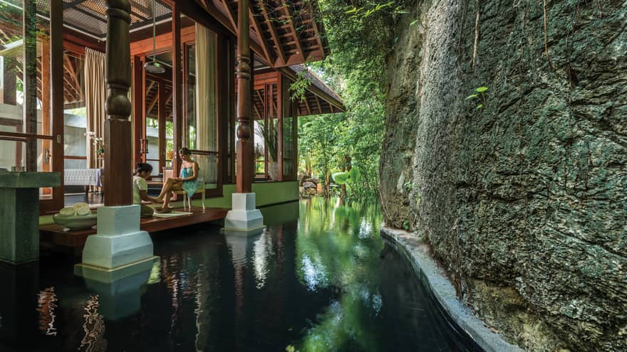 Woman gets foot massage on deck of Geospa by pool, large rock wall