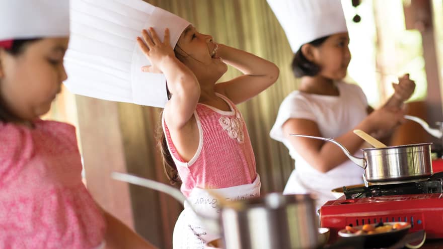 Three young children wearing tall white chef's hats in cooking class