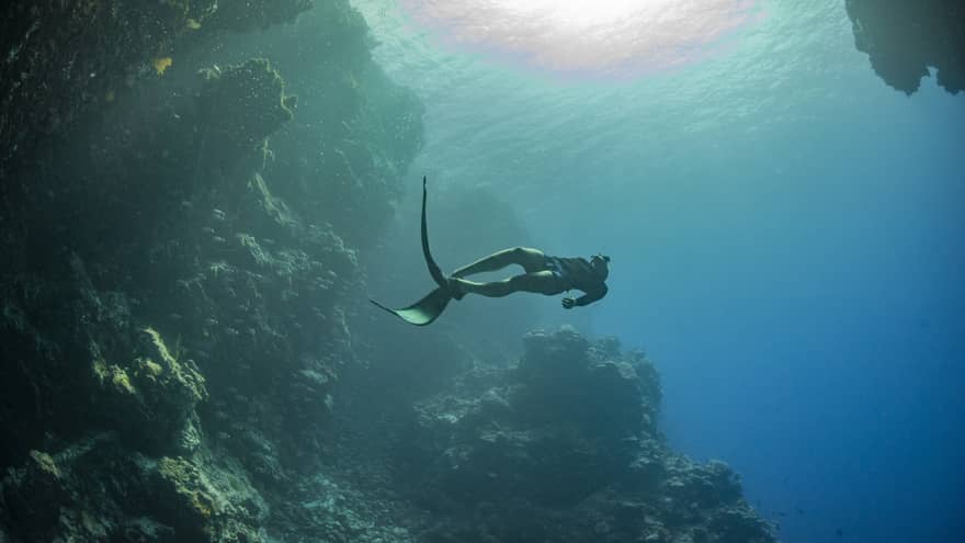 Scuba diver swims near a cave underwater