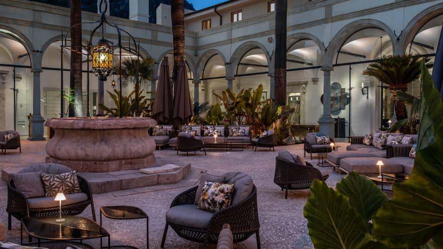 Outdoor hotel courtyard at dusk featuring chairs, tables and a central fountain, creating a serene lounge atmosphere