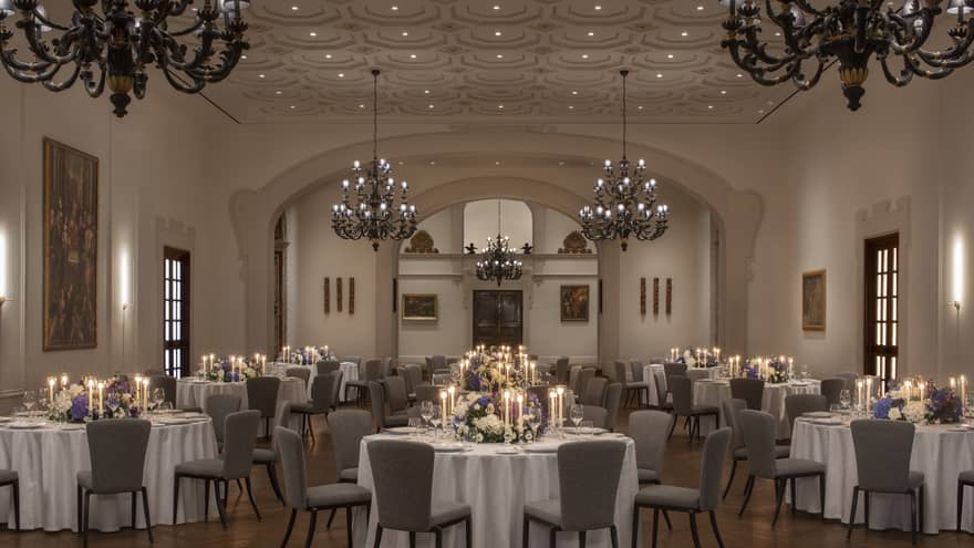 Elegant ballroom with round tables and chairs arranged for a wedding, adorned with large chandeliers above