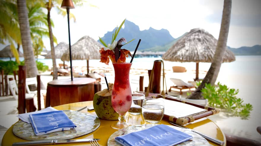 Fruity cocktail with tropical flower garnish on patio dining table by Bora Bora lagoon