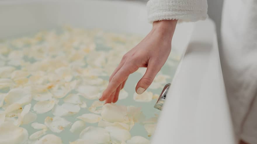 A person's hand touches the delicate white flower petals in a bath