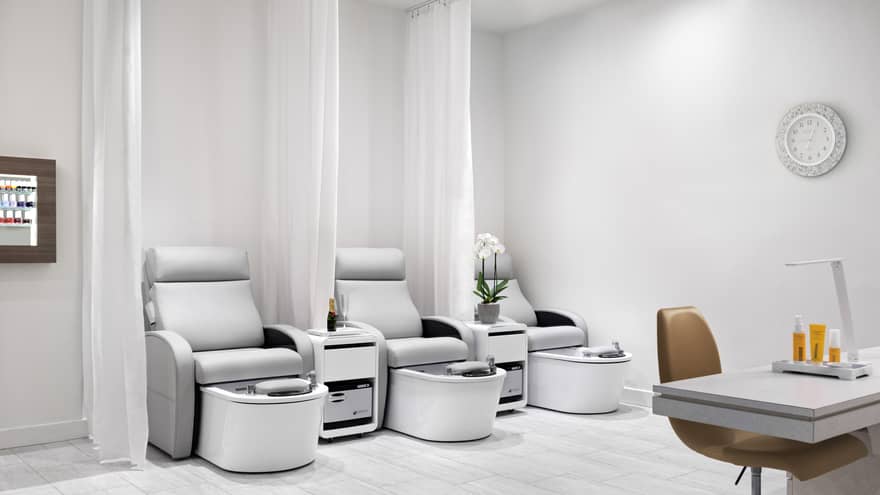 Nail salon with three light grey pedicure chairs, separate by white curtains, and one manicure station