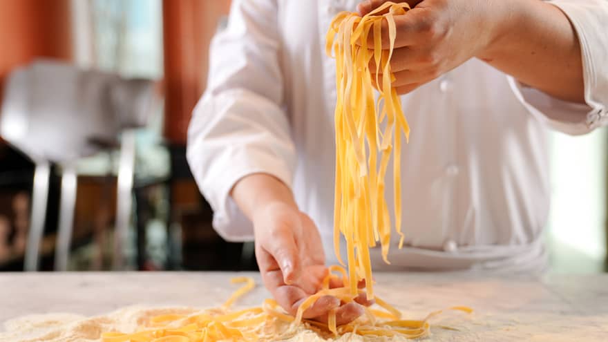 Close up of chef's hands holding a handful of pasta with flour and more pasta on the table below