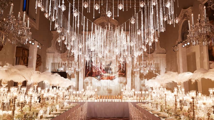An elegant wedding reception featuring chandeliers, crystal lights, tall candles and white feathers on the tables
