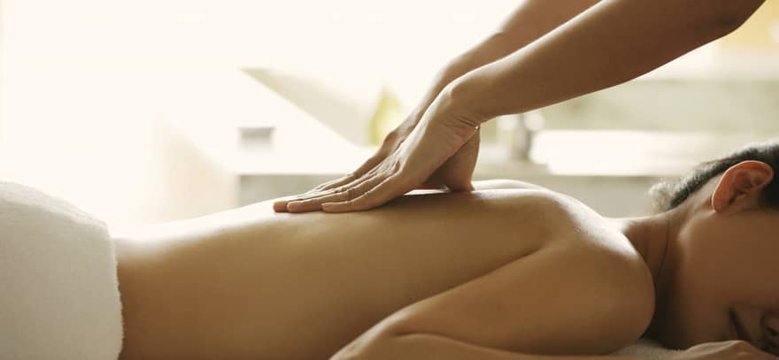 Masseuse reaches over, massages woman's bare back as she lies on spa table