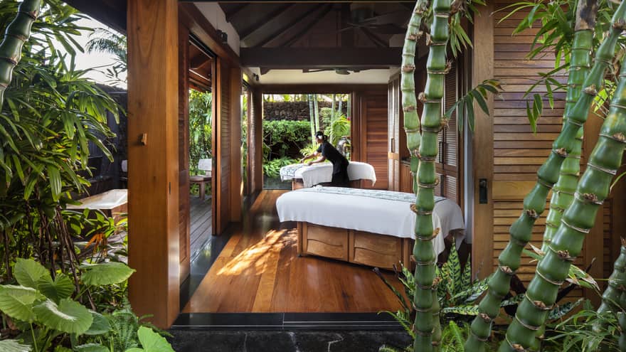 Spa staff spreads sheet on couples massage beds on open-air pavilion 