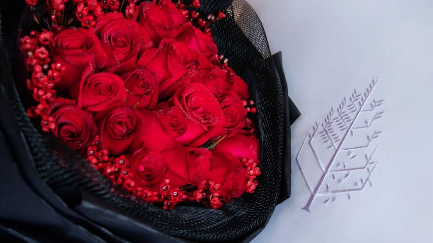 Bouquet of red roses wrapped in black fabric laying on a white pillow with the Four Seasons logo