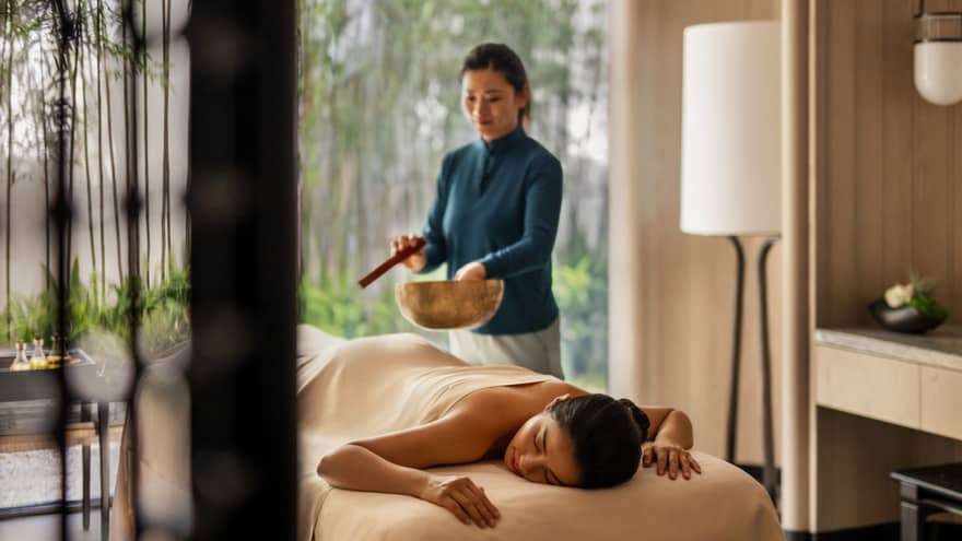 Female spa therapist performs singing bowl spa ritual for woman on spa treatment table and luxury hotel spa