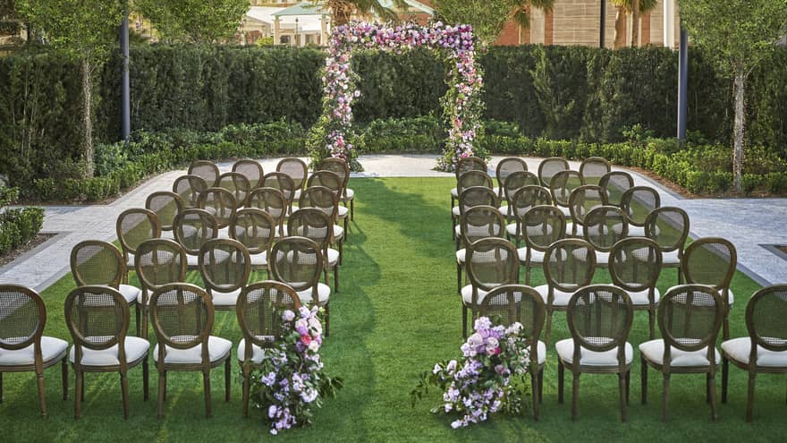Lawn set up for wedding ceremony with rows of chairs, flower arch and rounded hedges