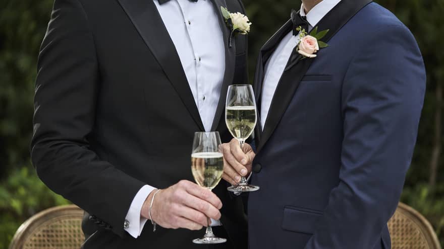 Two men drinking wine while holding each other.
