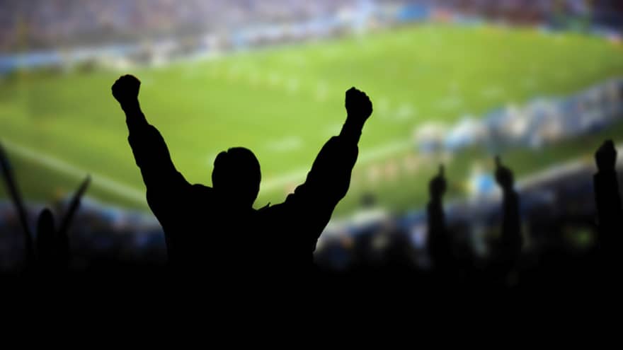 A silhouette of a person cheering at a football stadium.