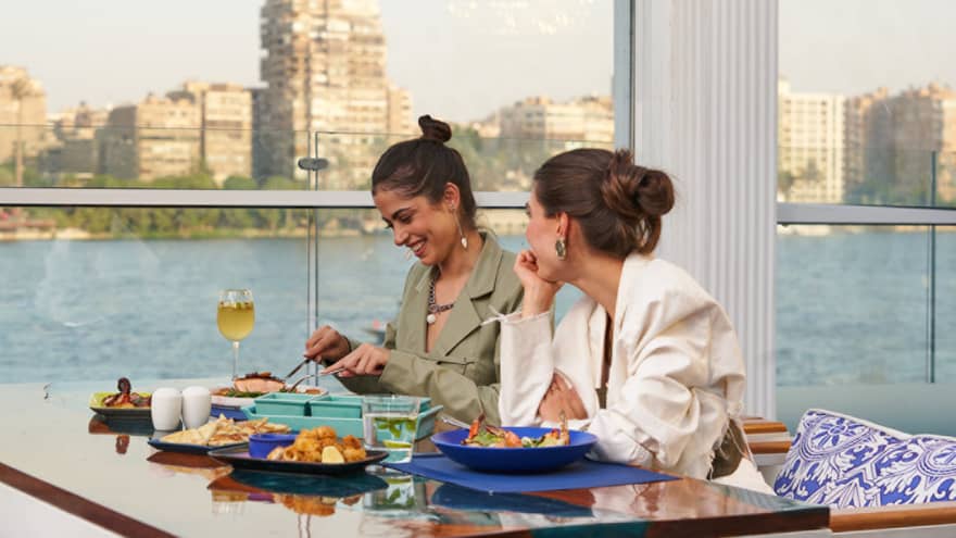 Two smiling people enjoy a seafood dinner at a restaurant with river views