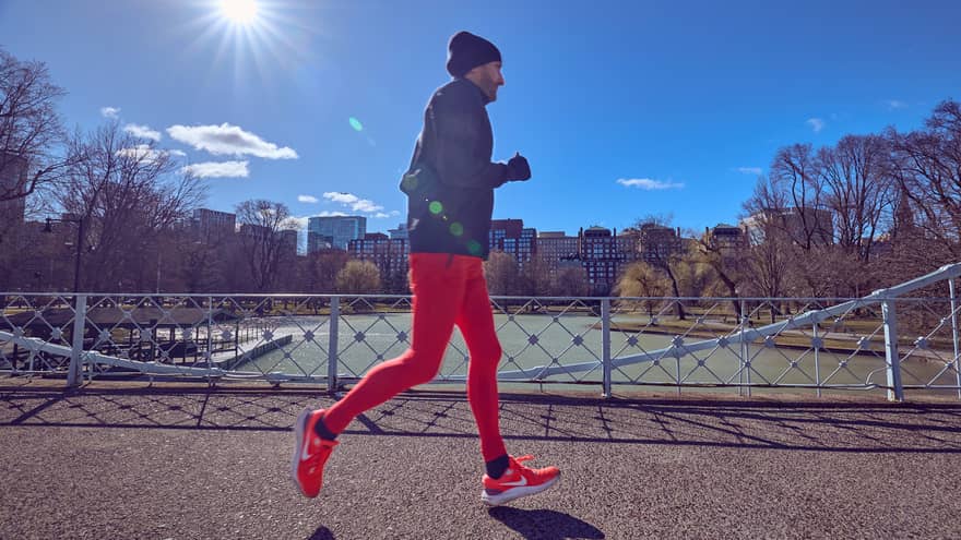 Chef Patrice running over a Boston bridge wearing bright-red jogging pants, bight-red shoes and a dark hoodie and hat