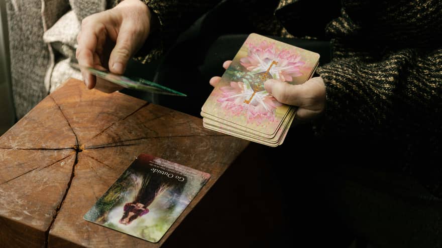 A pair of hands with a deck of tarot cards in one hand and the other holding a single card