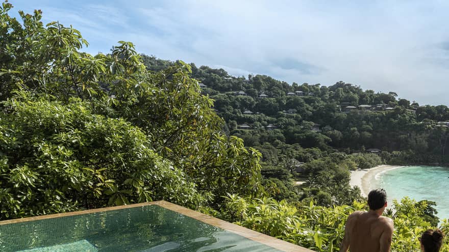 A couple looks out at a view of crystal blue waters and cliffs from an infinity pool