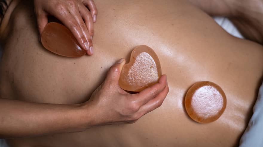 Three stones are placed on the exposed back of a client. The stones are a rectangle, heart and circle respectively.