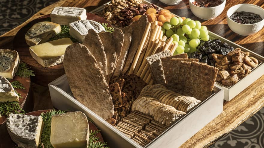 A charcuterie board with crackers and bread, a variety of cheeses, fresh and dried fruit, jams and nuts