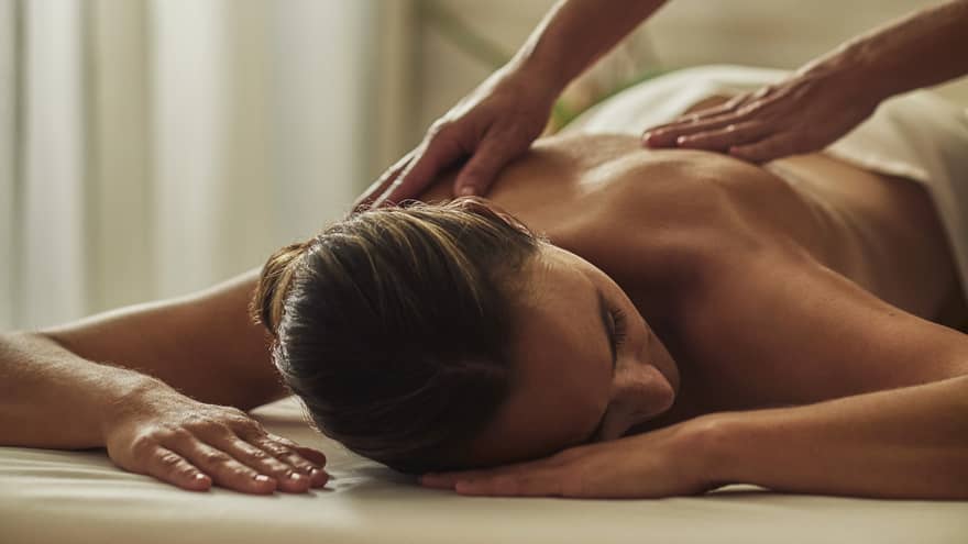 Woman in black uniform massages bare shoulders of woman lying on table face-down with head to side