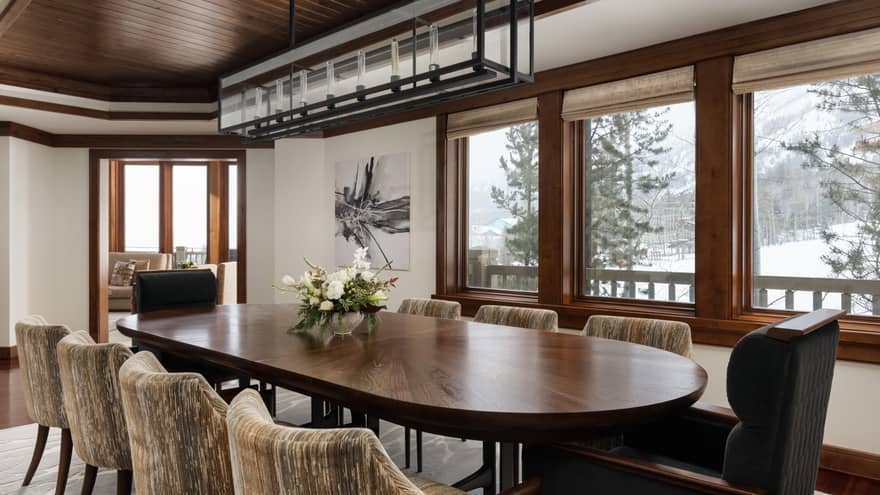 Dining room with a large dark wooden table, upholstered chairs, floral centrepiece, rectangular chandelier and snowy mountain view