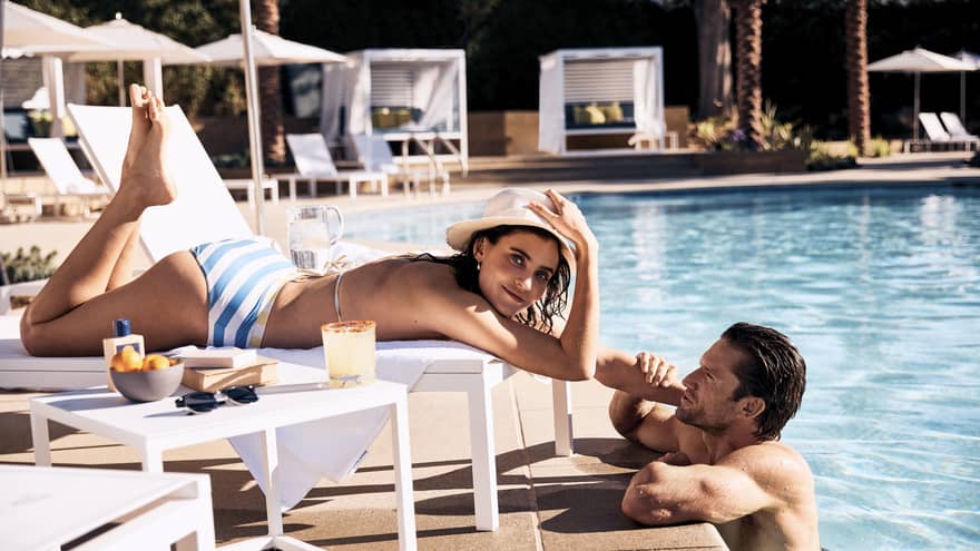 Guest laying in a lounge chair by the pool while the other guest stands in the pool.