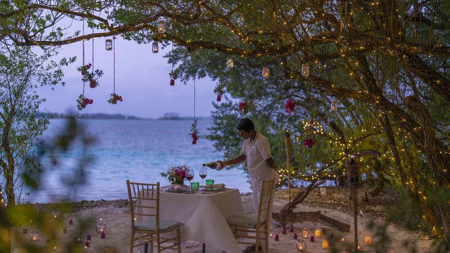 Resort staff pours wine into glass on beachside table set for two
