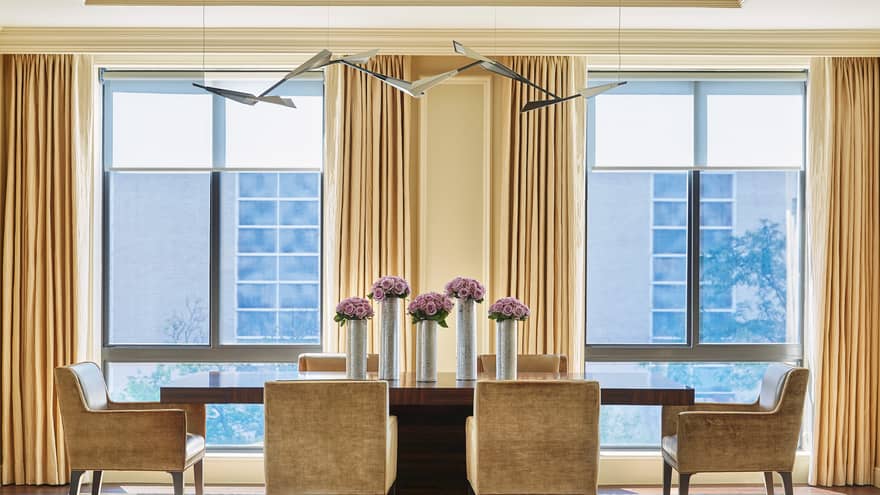 Imperial Suite modern dining table with golden brown velvet dining chairs around long wood table with tall silver vases, purple flowers