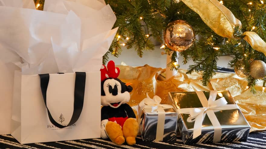 Various presents tucked under a Christmas tree decorated with gold onaments and ribbons