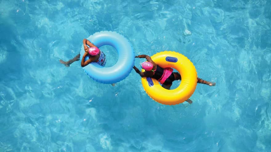 Aerial view of two swimmers in pink caps floating in blue and yellow inner tubes 