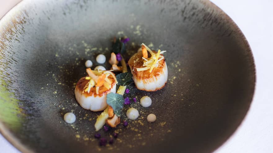 Two grilled scallops artfully garnished in a black bowl